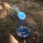 Eine PET-Flasche, die zur Fertigung eines Wasserfilters vorbereitet wurde. Im Deckel ist ein kleines Loch als Abfluss eingearbeitet. Der Flaschenboden ist abgetrennt und dient wahlweise als Auffanggefäß oder zum Eingießen des Schmutzwassers.